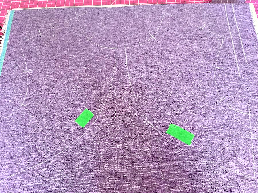 Purple fabric with sewing pattern lines. Two pieces of green painter's tape are placed on the fabric to mark the wrong side for easy identification during sewing.