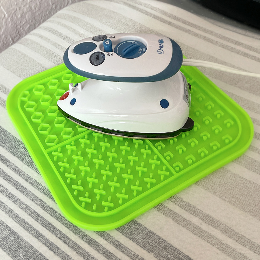A small white iron resting on a bright green silicone trivet, used as a heat-resistant surface to safely hold the hot iron.