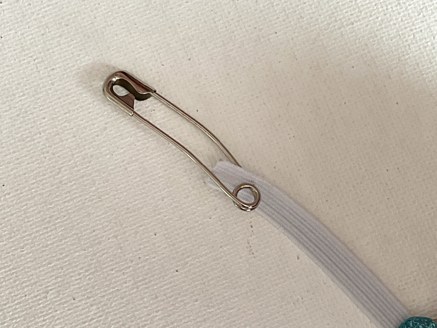 A metal safety pin attached to the end of a white elastic band.