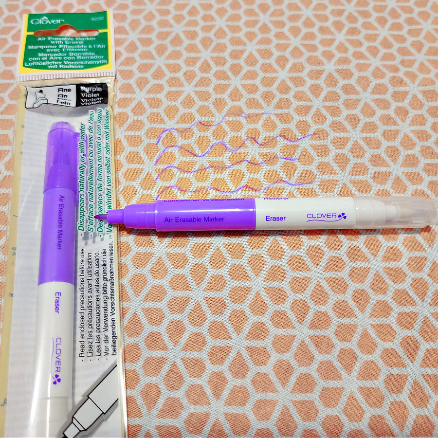 Image of a clover marking pen in it's original package and another pen laying open on a piece of fabric with some pencil marks on it