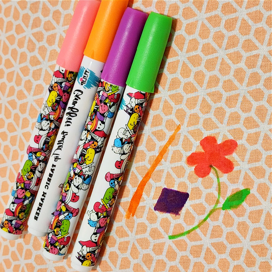 four fabric flower markers of various colors and a flower design on a piece of fabric drawn as example