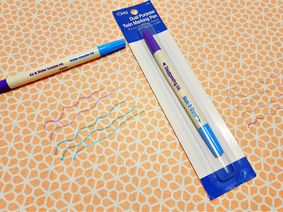 Image of a Dritz blue and purple marking pen in it's original package and another pen laying on a piece of fabric with some pencil marks on it
