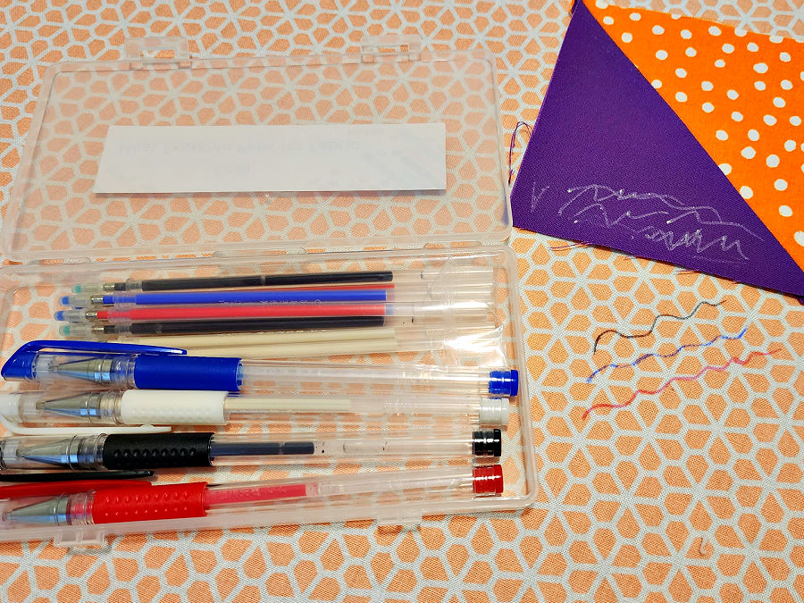 madame sew heat erasable marking pen set laying on a piece of fabric with a half square triangle visible. there are pencil marks of various colors visible both on the fabric and on the half square triangle