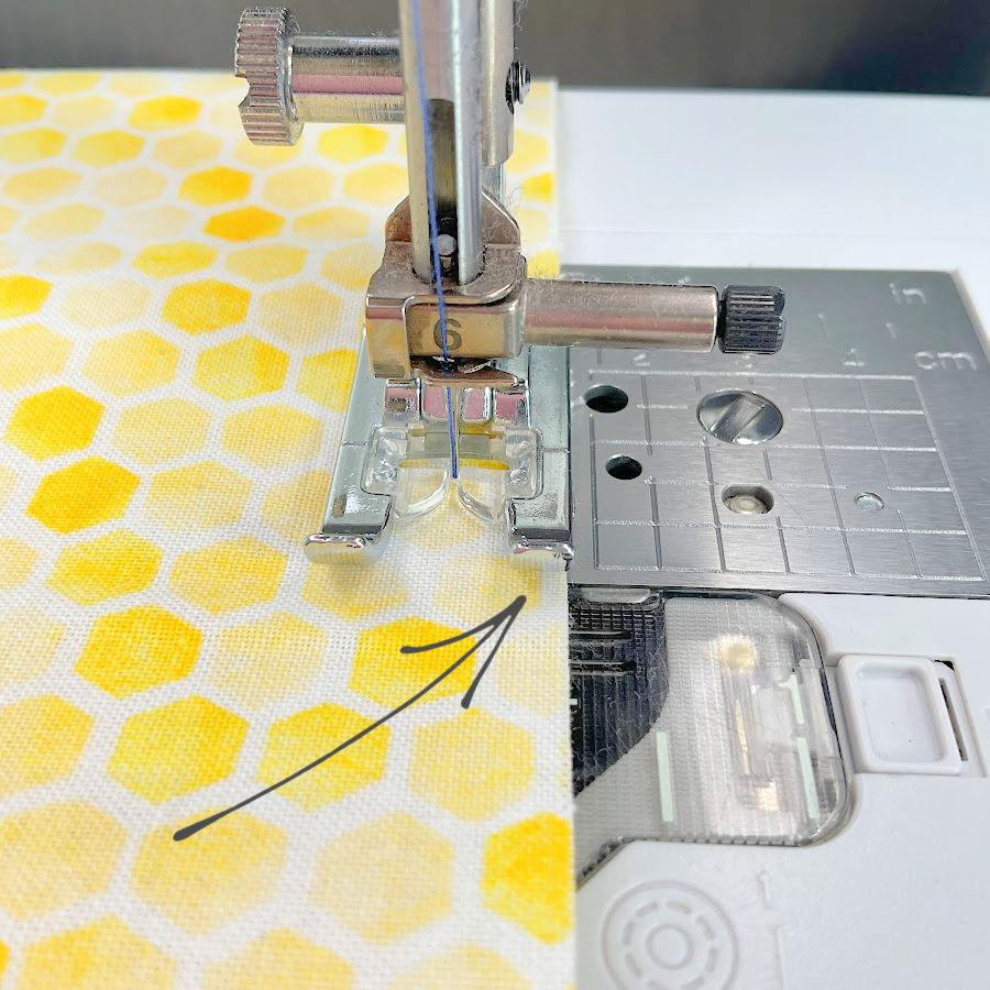 Image shows the fabric on a sewing machine aligned with the edge of the presser foot as a guide