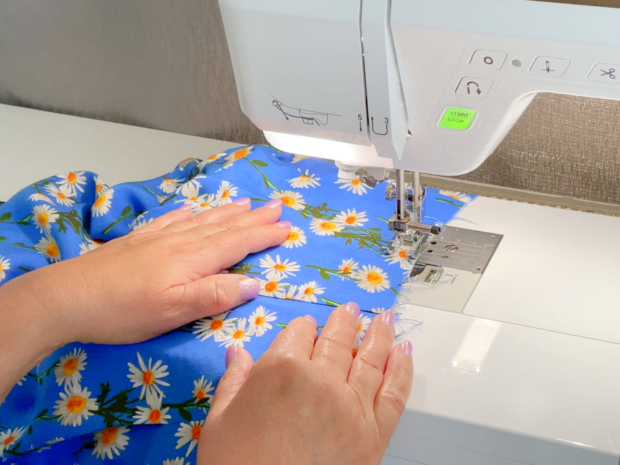 a woman's hands guiding the fabric while sewing a seam on a sewing machine