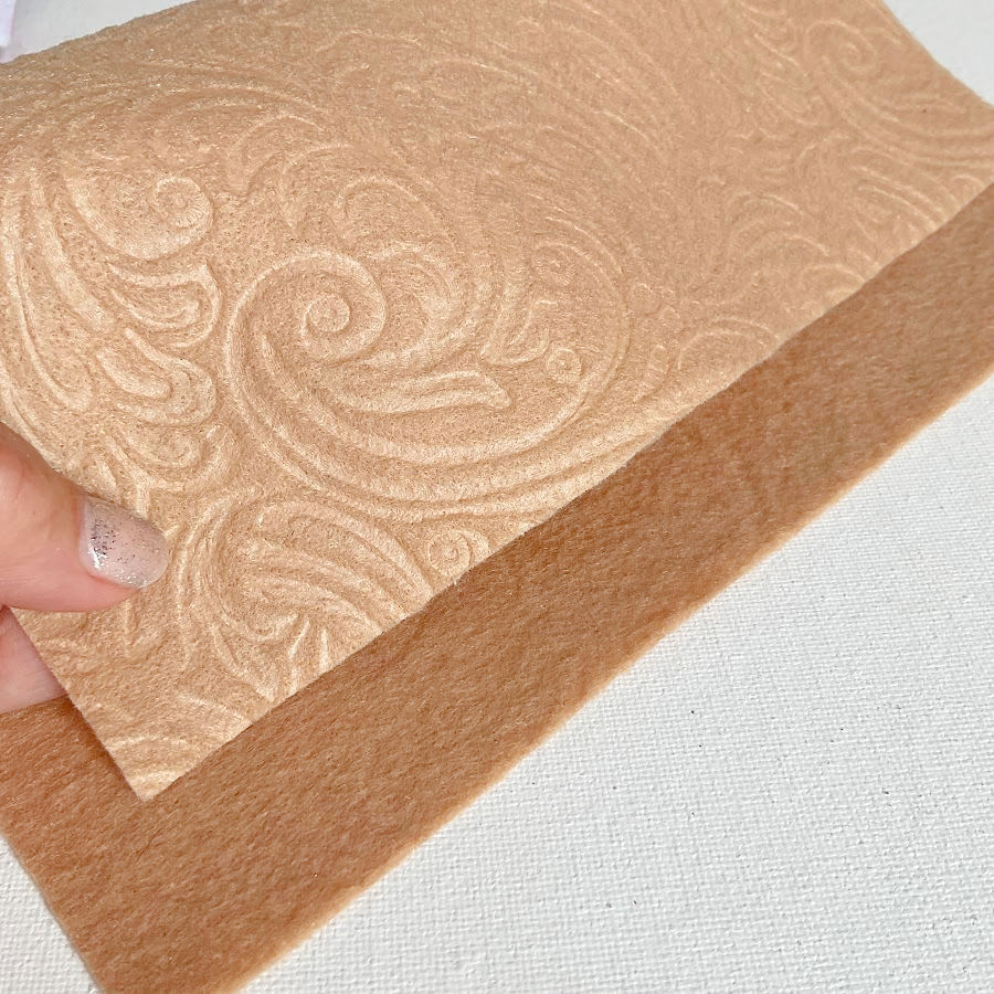 a woman's hand holding a piece of felt embossed with a floral design