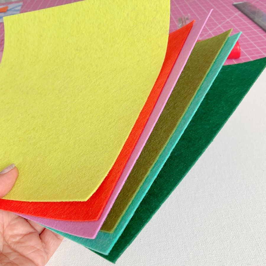 a woman's hand holding sheets of multi colored stiff felt