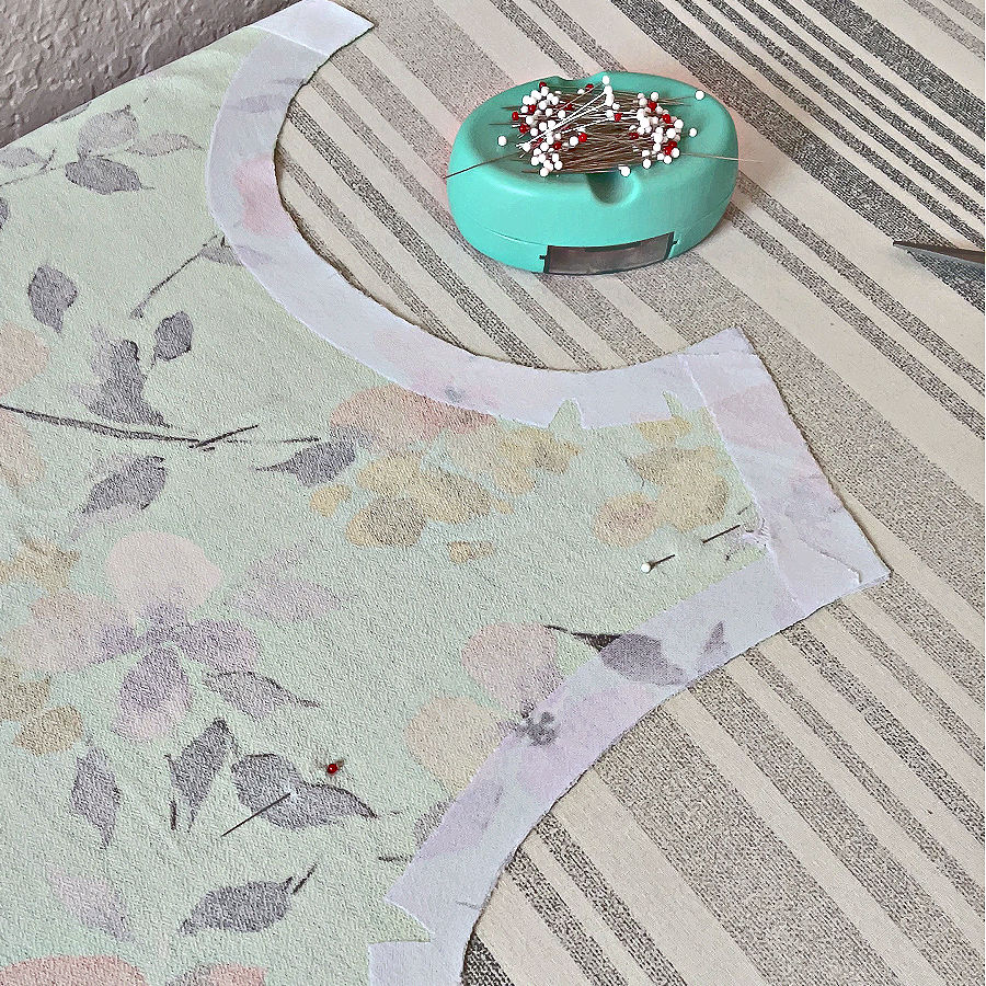 a piece of garment with knit stay tape around the neckline already applied and some pins inserted a magnetic needle holder in the background