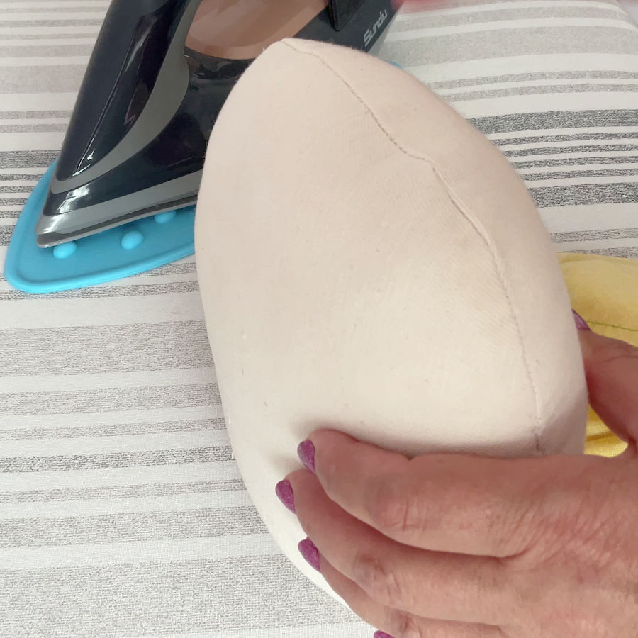 a woman's hand holding a tailors ham with an iron in the background