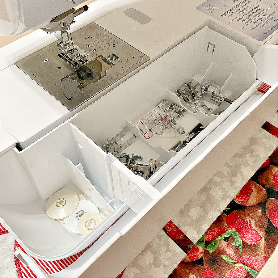 a sewing machine showing th eneedle assembly and the storage compartment for small items with the lid open for inspection