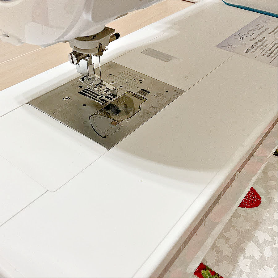 A sewing machine showing the needle assembly and the storage compartment for small items with the lid closed