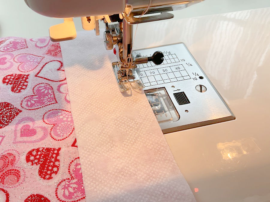a sewing machine needle assembly while sewing a white strip of fabric onto a colored strip in step 1 of making the fabric angels