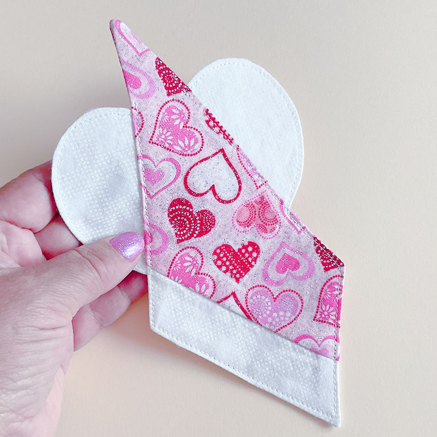 a womans hand holding the fabric angel after the final topstitching and pressing