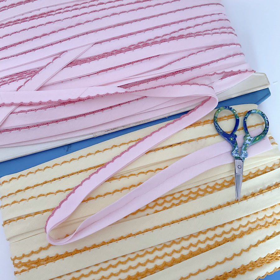 pre-made binding of various colors with a decorative edge a pair of detrail scissors sitting on top