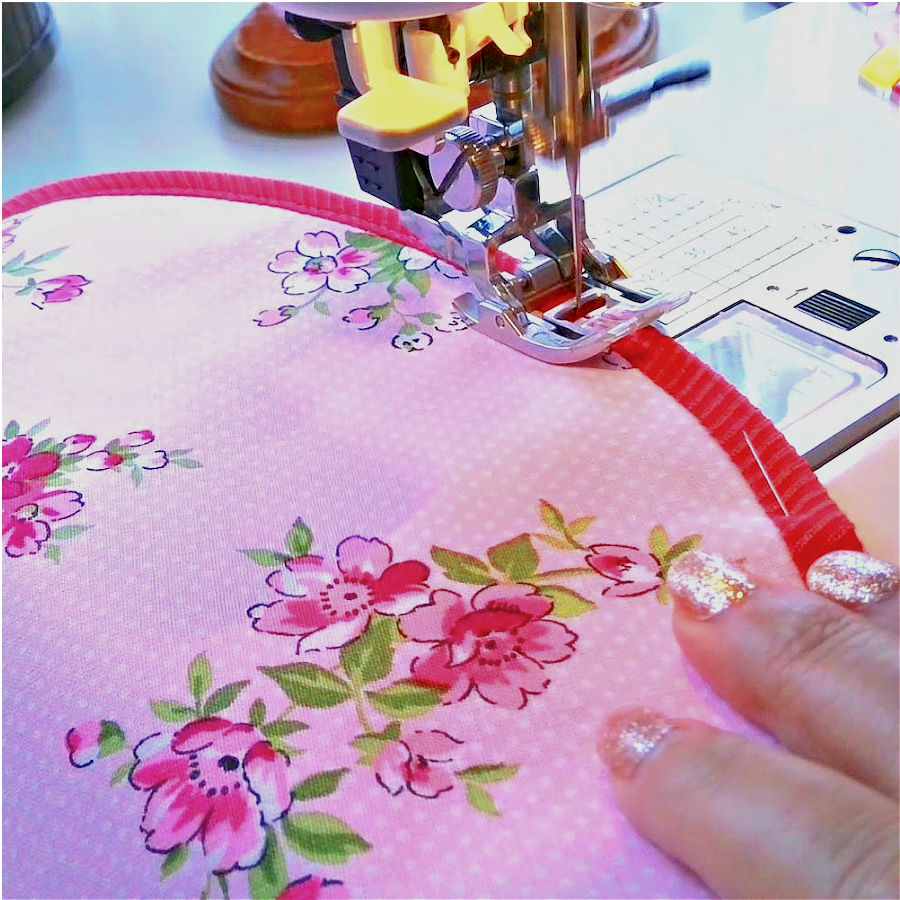 a sewing machine needle assembly sewing bias binding on a curved line. a womans hand is guiding the fabric