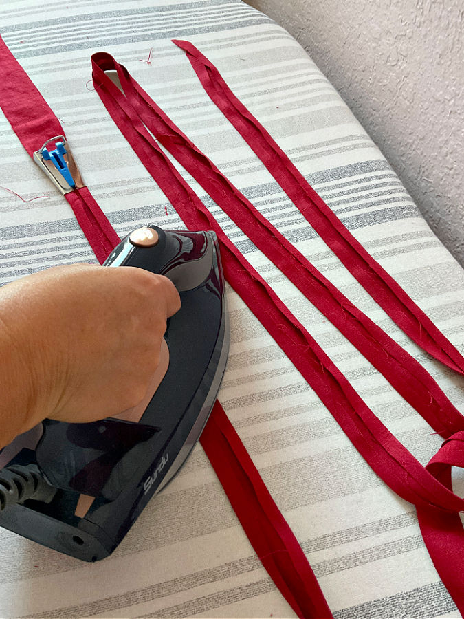 a womans hand ironing strips of binding while they are being made