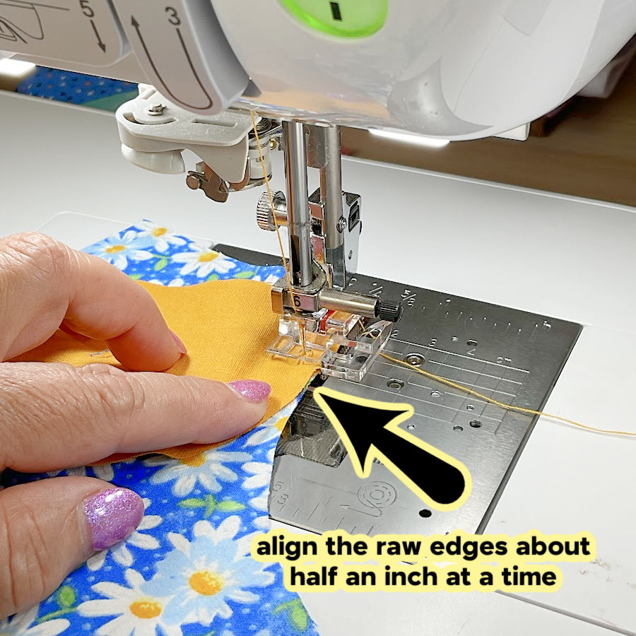a womans hand holding the fabric layers while sewing and an arrow pointing to the alignment of the pieces of fabric the text "align the raw edges about half an inch at a time" superimposed on the image