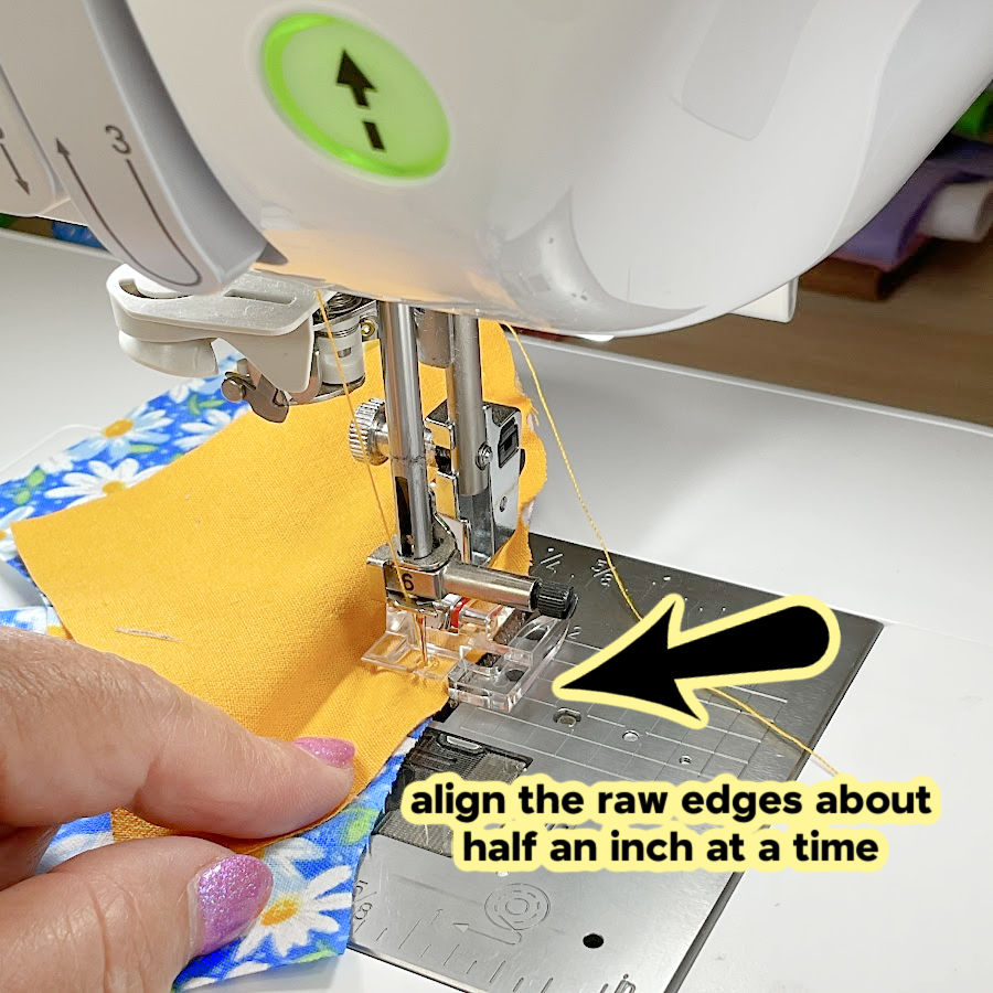 a womans hand holding the fabric layers while continuing sewing and an arrow pointing to the alignment of the pieces of fabric the text "align the raw edges about half an inch at a time" superimposed on the image