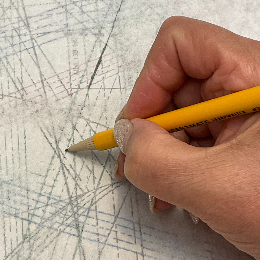 a woman's hand holding a pencil while tracing lines on a complicated pattern