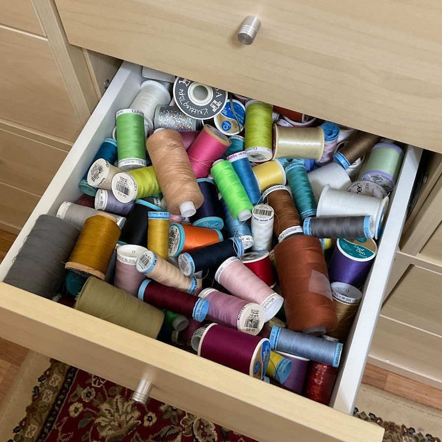 a storage drawer full of thread spools and cones of various colors in complete disarray