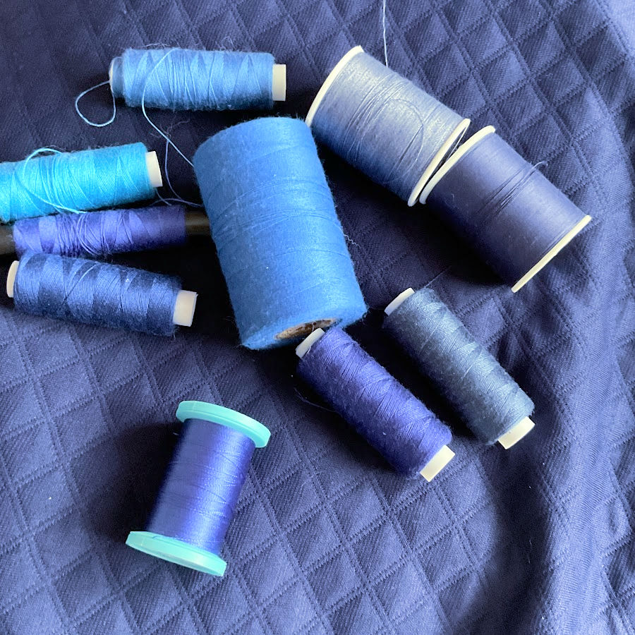 ten spools of thread of various shades of blue sitting on a blue mat