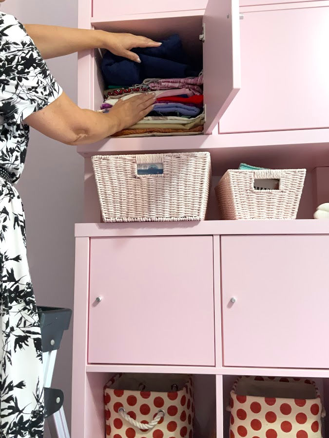 a woman partially seen looking at a storage compartment full of fabric pieces. straw storage containers are also visible in the image