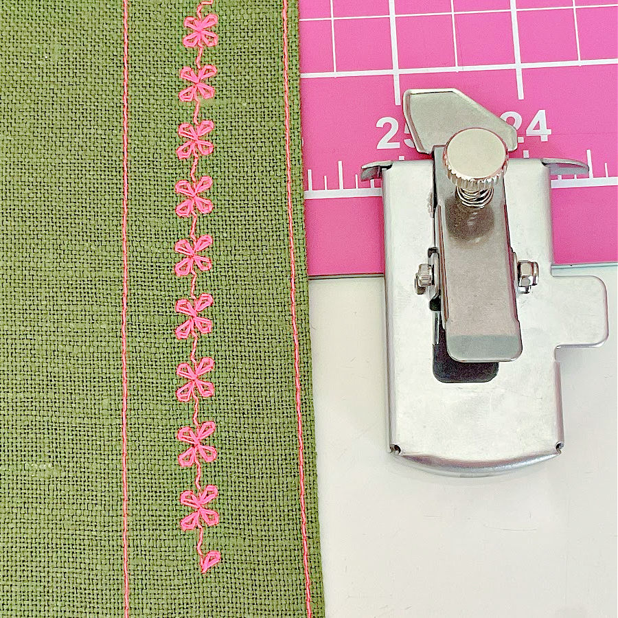 the magnetic seam guide sitting on a cutting mat with a piece of fabric having a decorative stitch and two straight stitches on it