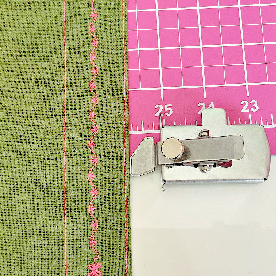 the magnetic seam guide sitting on a cutting mat with a piece of fabric having a decorative stitch and two straight stitches on it