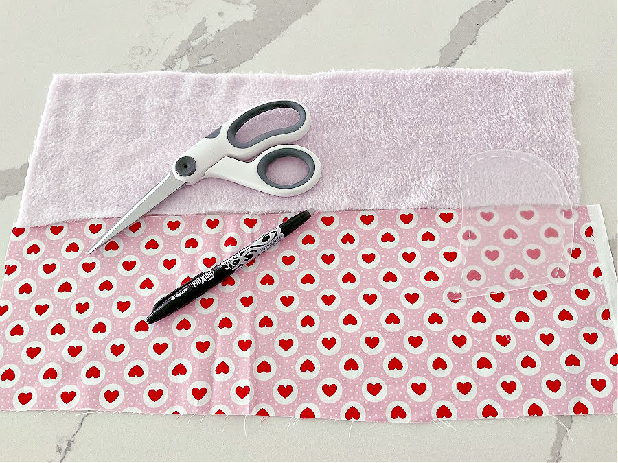two pieces of fabric prepared to be sewn together for cutting the arms of the bear a frixion pen and a pair of scissors also