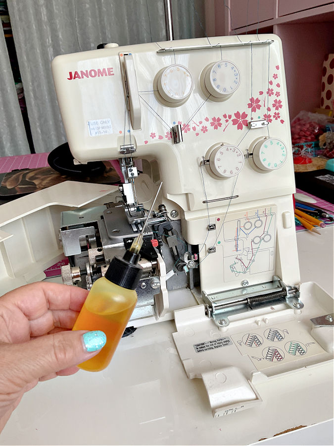 image of a janome serger overlock machine with the cover open in the foreground a womans hand holds a small bottle of oil