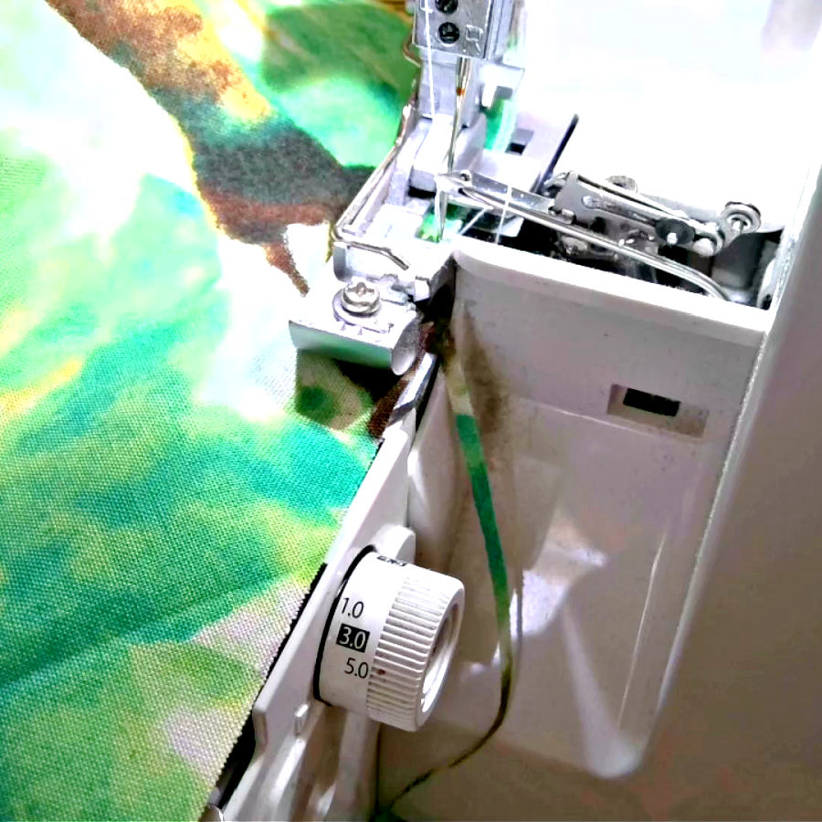 the serger overlock machine working with a thin strip of material being trimmed from the edge of the fabric