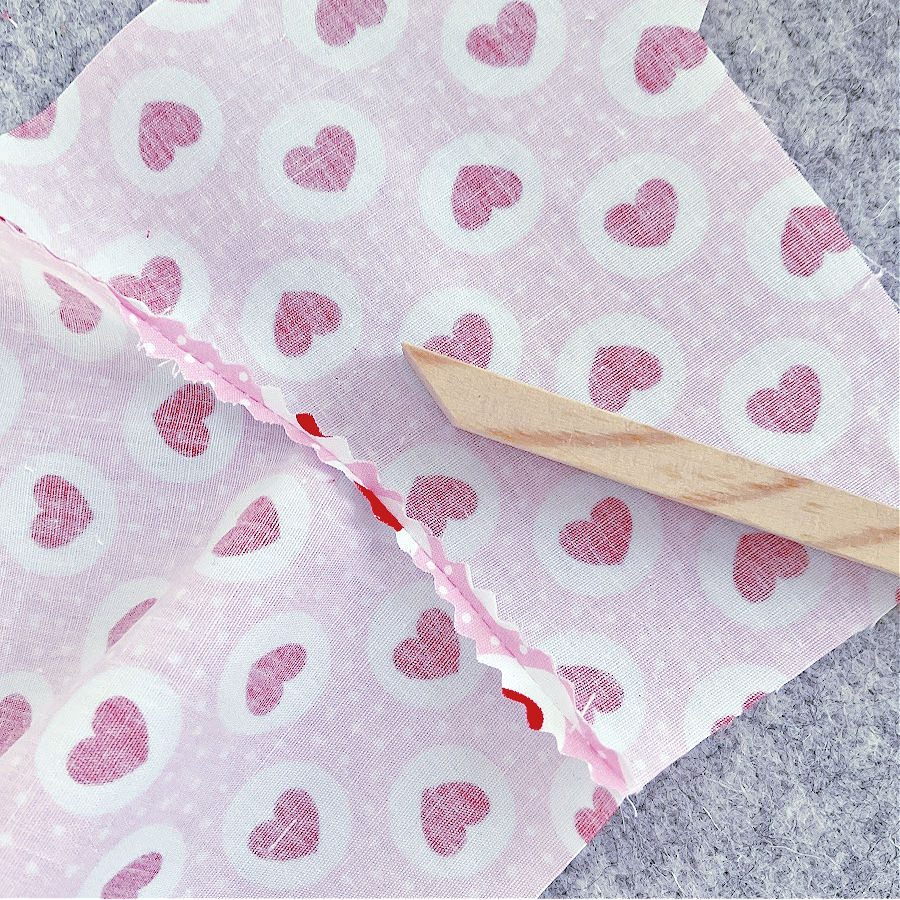 leg pieces of the bear stitched together and with the seam allowance cut with pinking shears a wooden pressing tool in the foreground