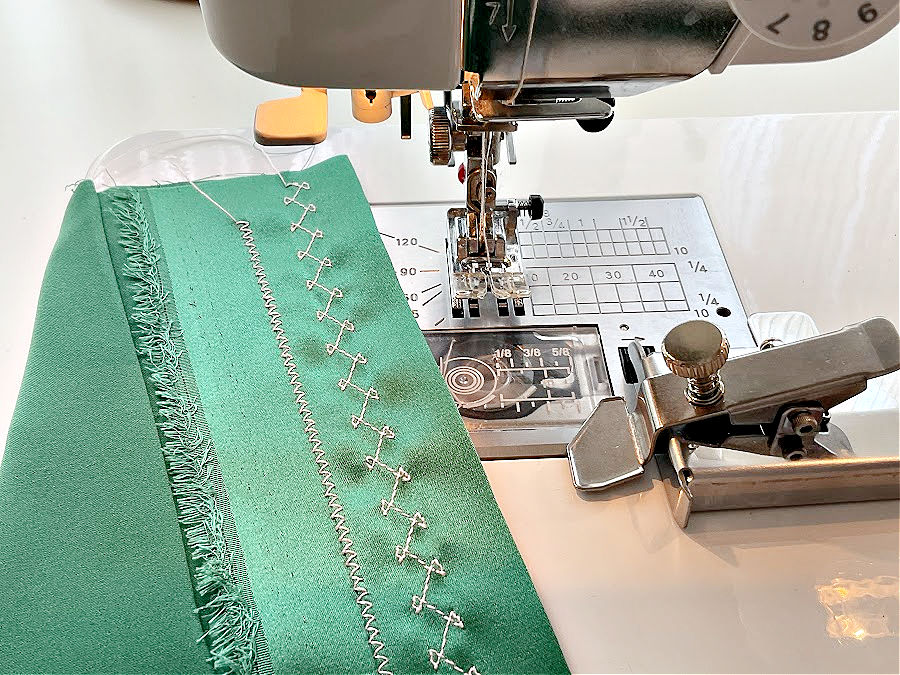 a decorative stitch on a green piece of silk sitting on a sewing machine with the seam guide nearby