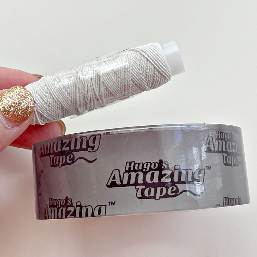 a womans hand holding an elastic thread spoo, wrapped in tape a roll of hugos amazing tape nearby