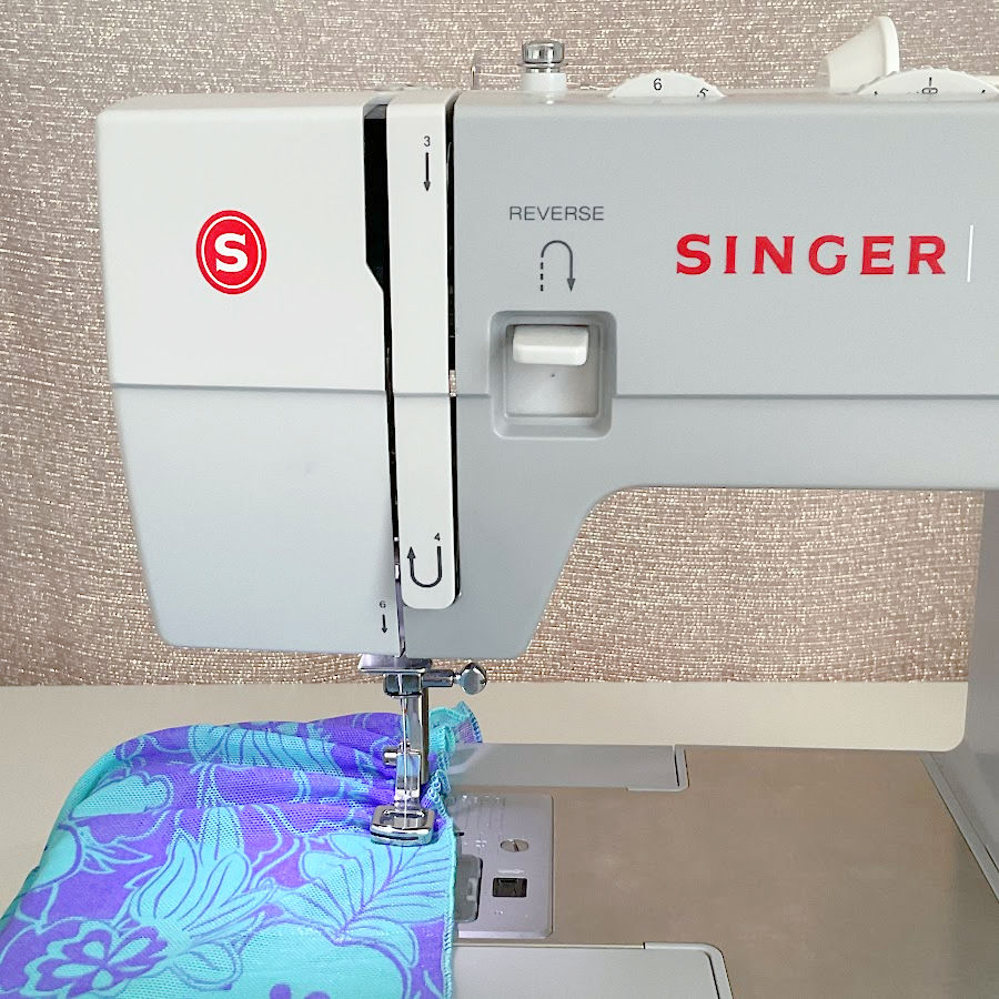 a singer sewing machine while sewing a piece of blue material with the low shank gathering presser foot attached