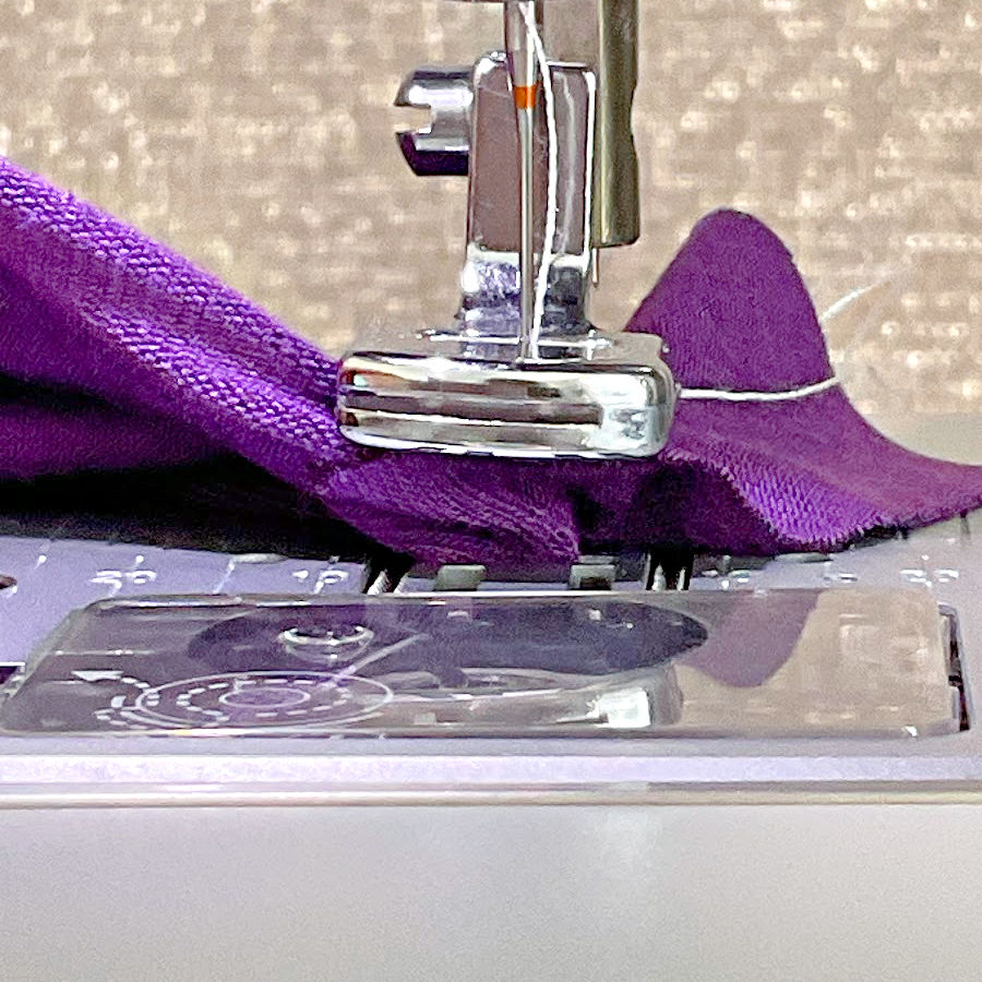 a piece of purple rayon knit fabric jammed in a sewing machine while using the gathering foot