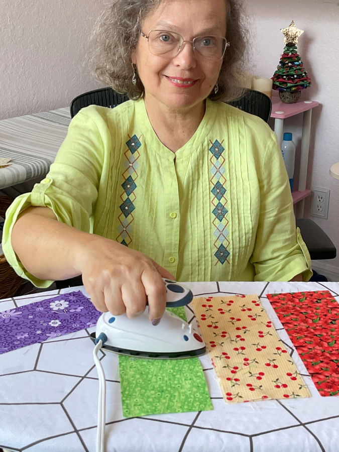 a woman using a mini iron to iron rectangular pieces of material on an ironing board