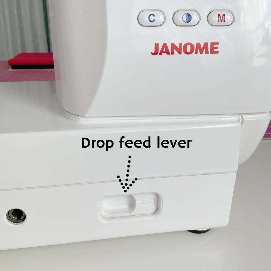 a janome sewing machine front panel detail with the drop feed lever highlighted by an arrow
