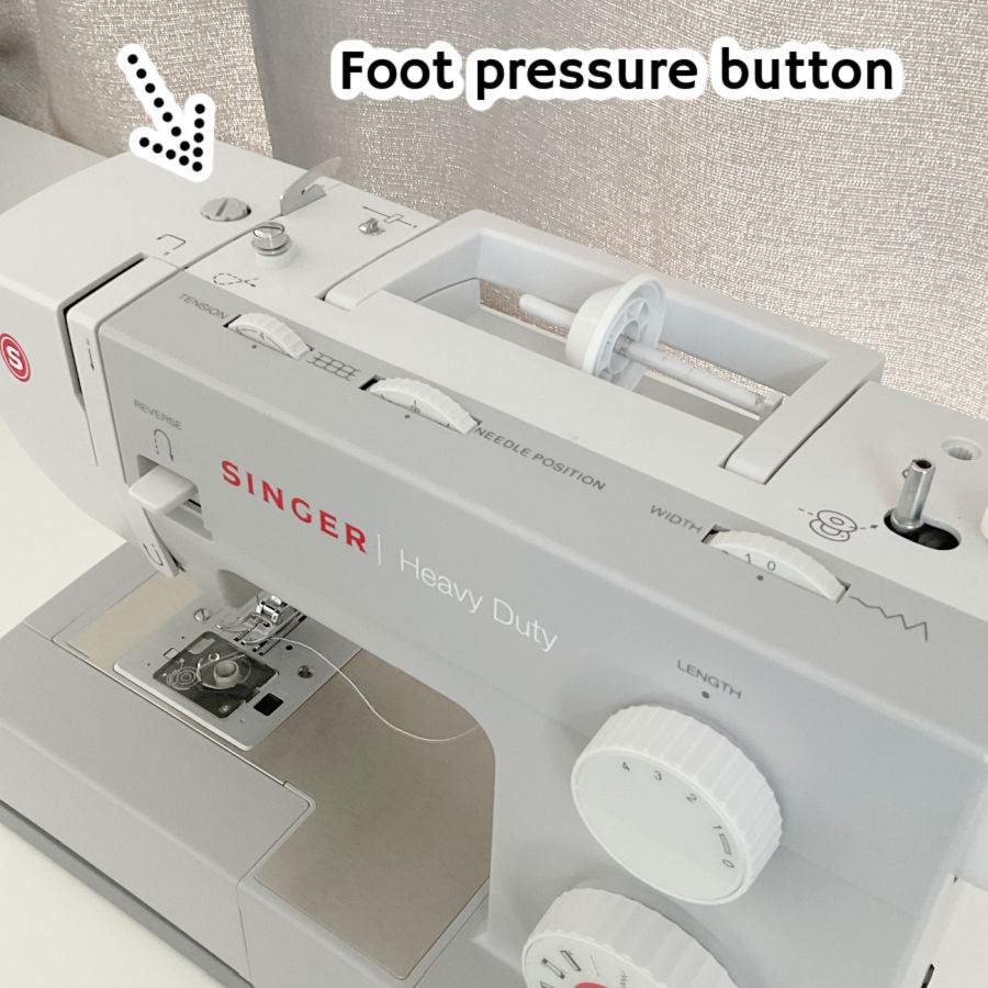 a singer heavy duty sewing machine seen from the top with the foot pressure button highlighted by an arrow which points at it