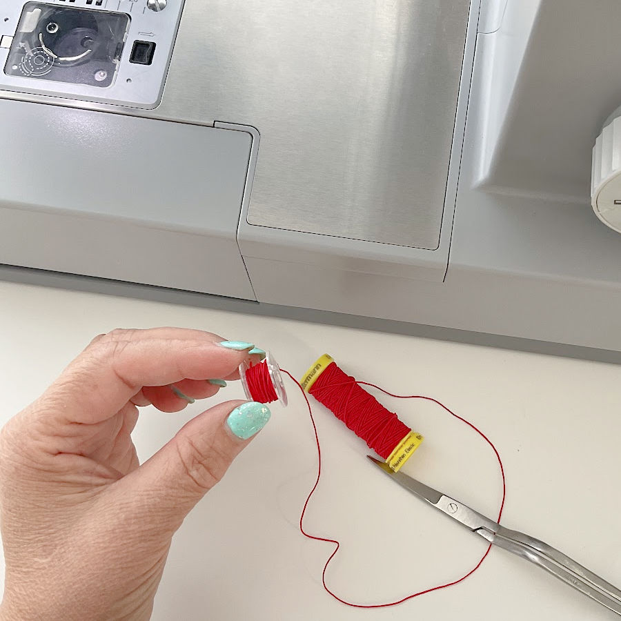 winding elastic thread on a bobbin a womans hand holding the bobbin the spool of thread is on the table
