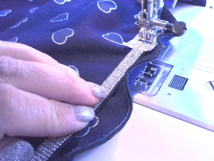 a sewing machine needle assembly while sewing elastic on a pair of shorts a womans hand guiding the elastic