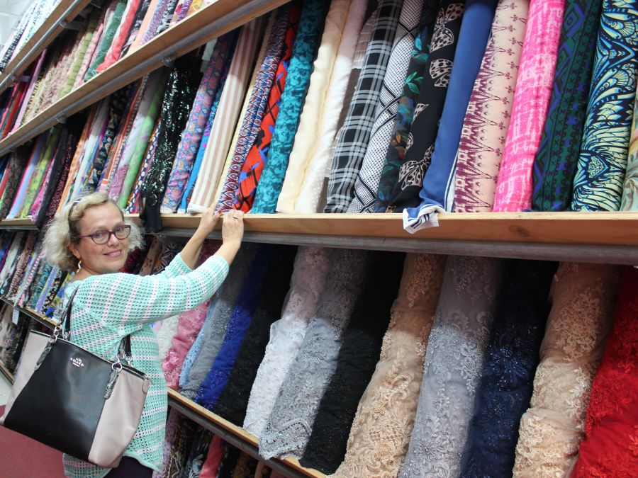 A woman in a fabric store looking at the camera with many rolls of fabric on display