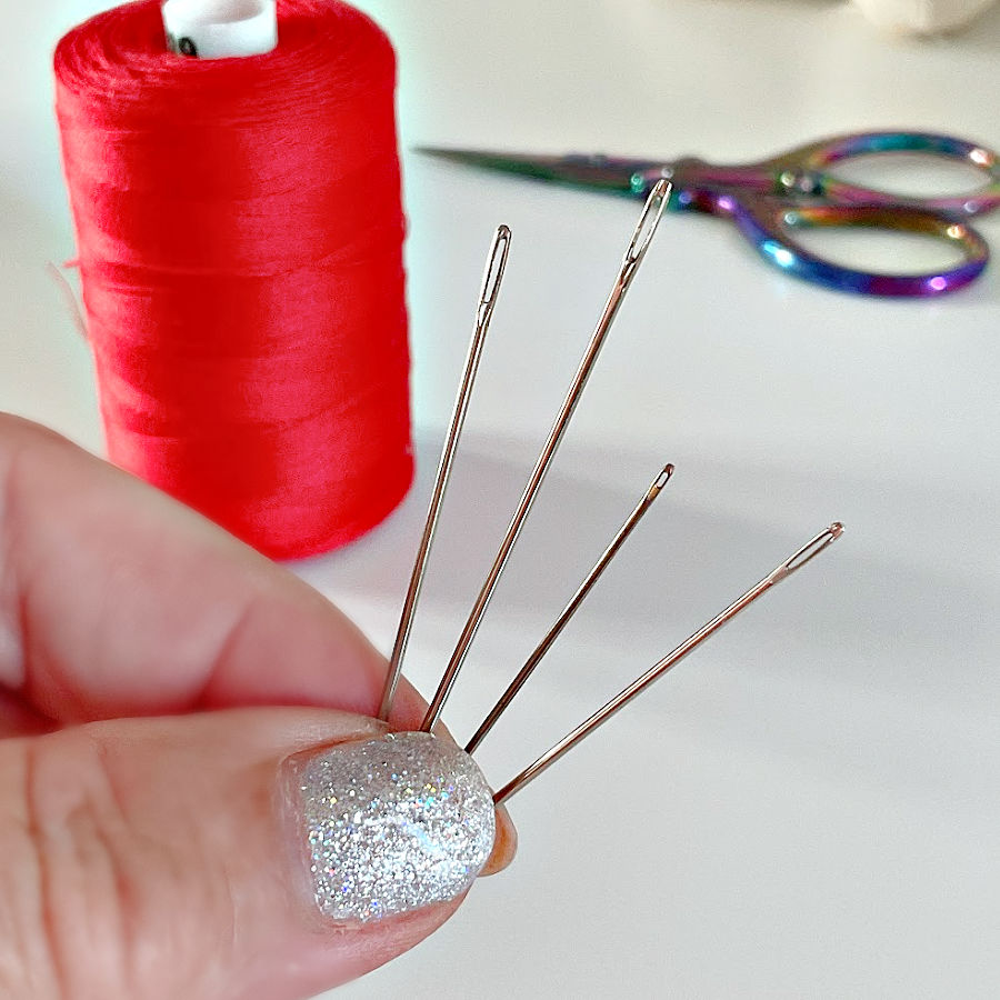 a close up of a womans hand holding four hand sewing needles