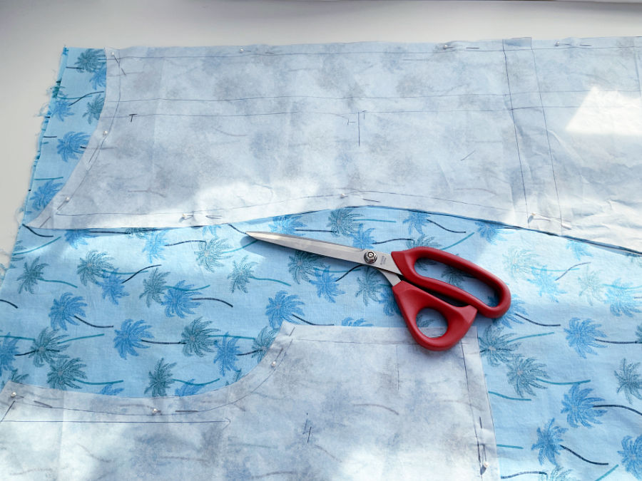 a pair of tailors scissors on a piece of material two paper pattern pieces affixed with pins to the material