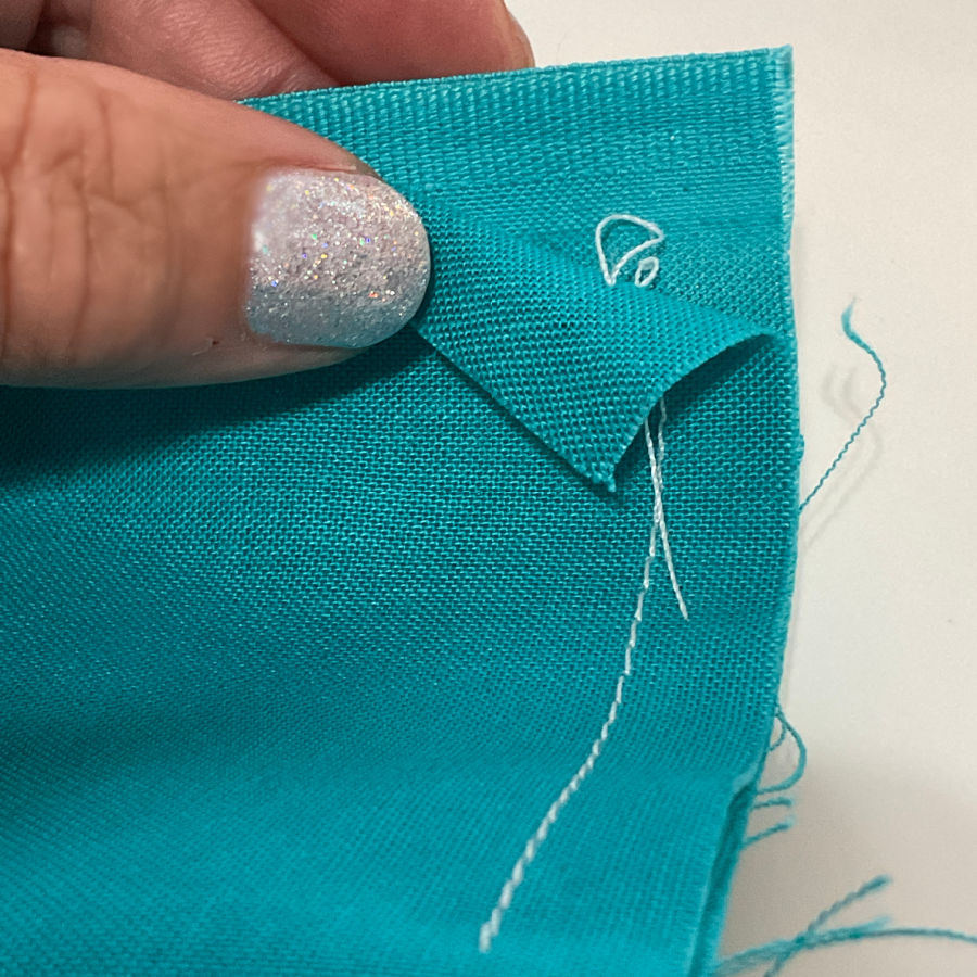 a womans hand holding a piece of material folded in such a way to show the thread tails at the end of the stitch on both sides of the fabric
