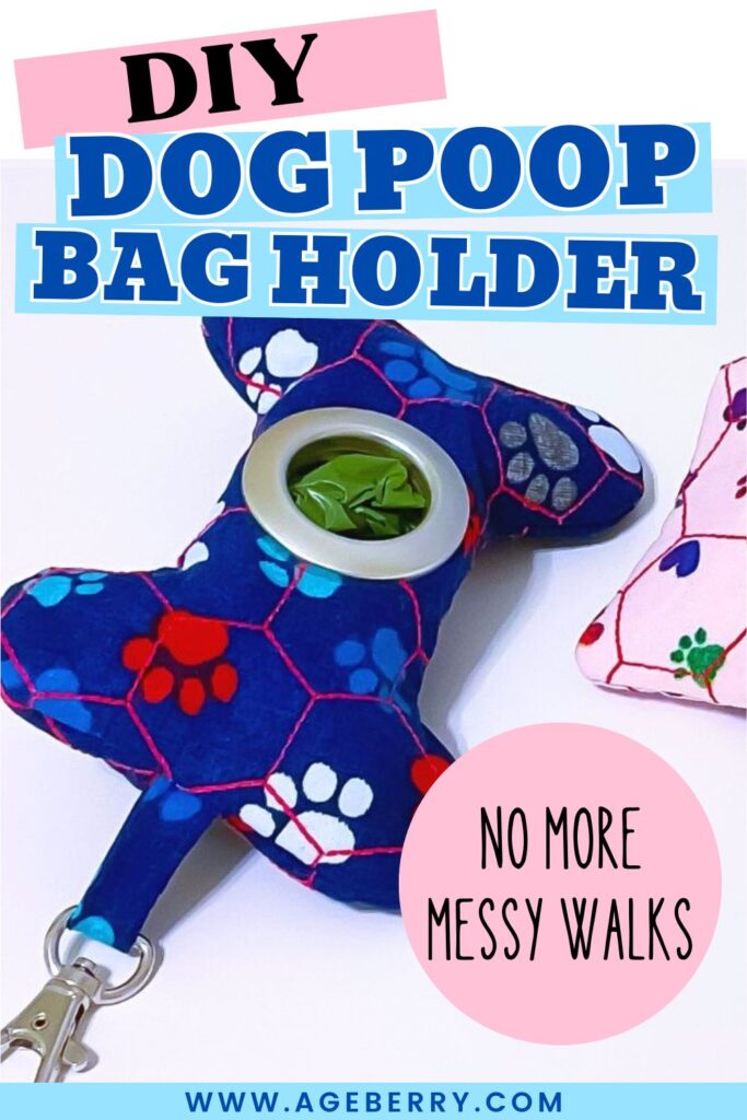 Handmade dog poop bag holder sewn from dark blue fabric with colorful paw prints, shaped like a bone with a round dispenser opening showing green bags inside. A silver clip is attached at the bottom, and a pink version of the holder with paw prints is partly visible on the side.
