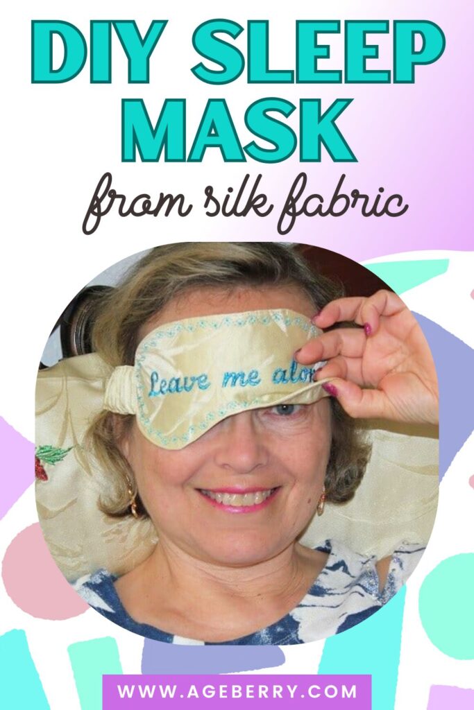 Woman smiling while wearing a handmade silk sleep mask embroidered with the words “Leave me alone.” The mask is light-colored silk with decorative stitching along the edges.