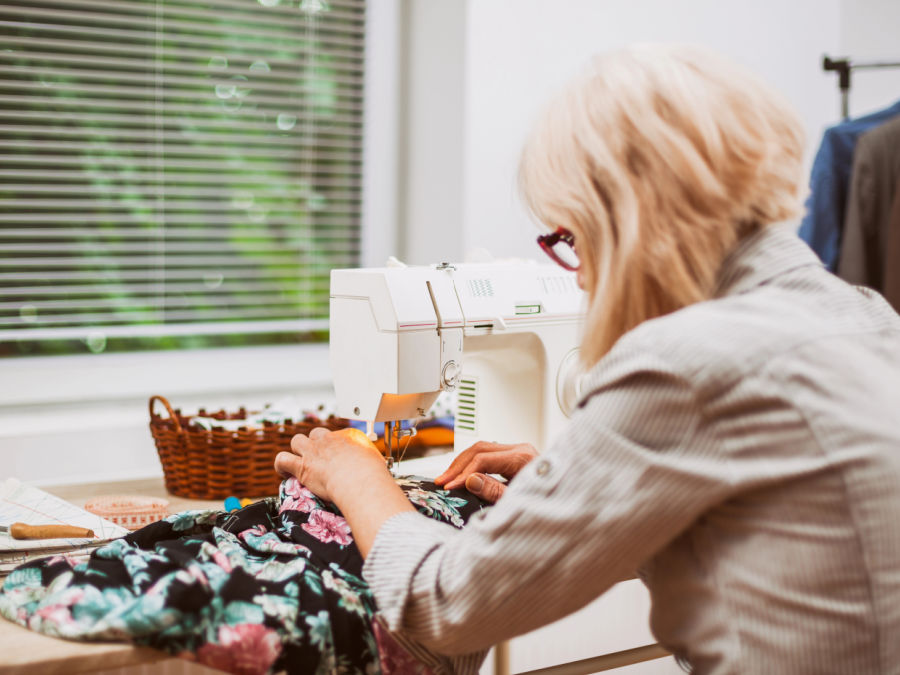 a woman working at a sewing machine seen from behind both hands are manipulating a piece of fabric