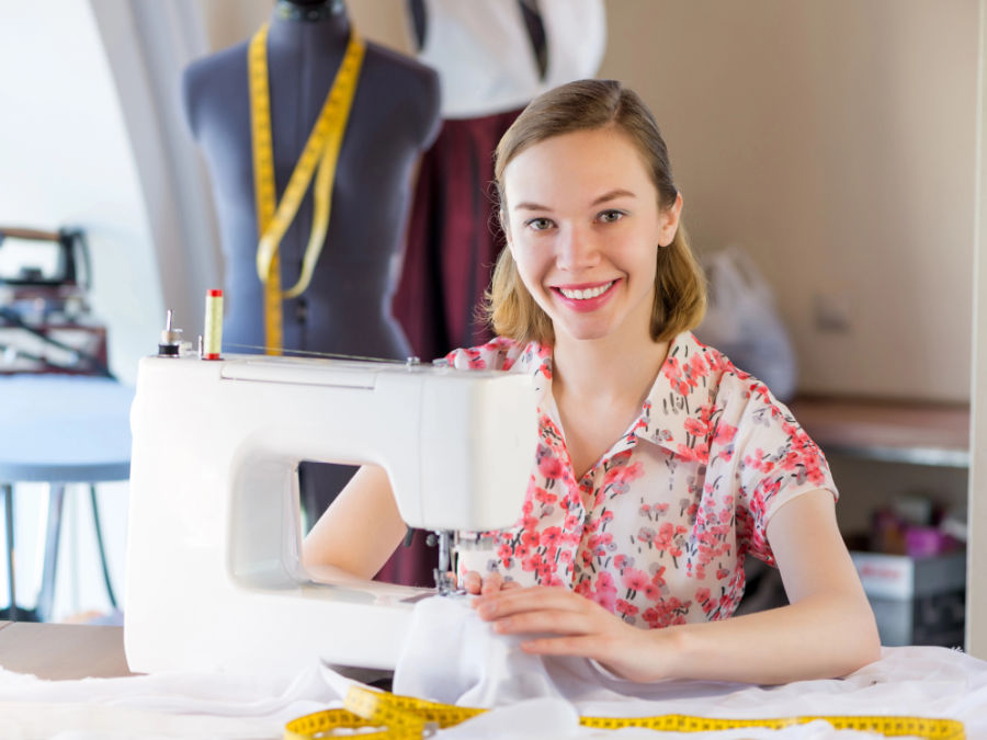 a woman working at a sewing machine smiling and obviously happe a mannequin and some measuring tapes in the background