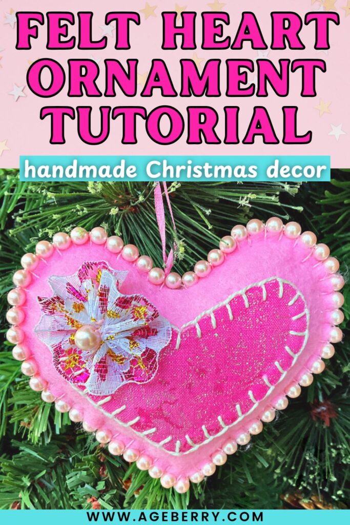 Close-up of a handmade pink felt heart ornament decorated with pearl trim, white blanket stitching, and a fabric flower with a pearl center. The ornament hangs on a Christmas tree.